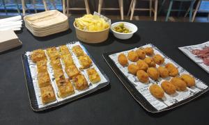 Fotografia del sopar preparat per la Fundació Ramon Noguera. Diferents safates amb pizza, truita de patates, fregits, olives i patates xips.